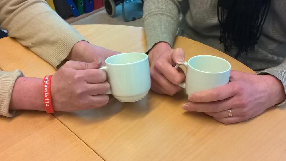 Kaksi ihmistä istuu kahvikupit kädessään pöydän ääressä.