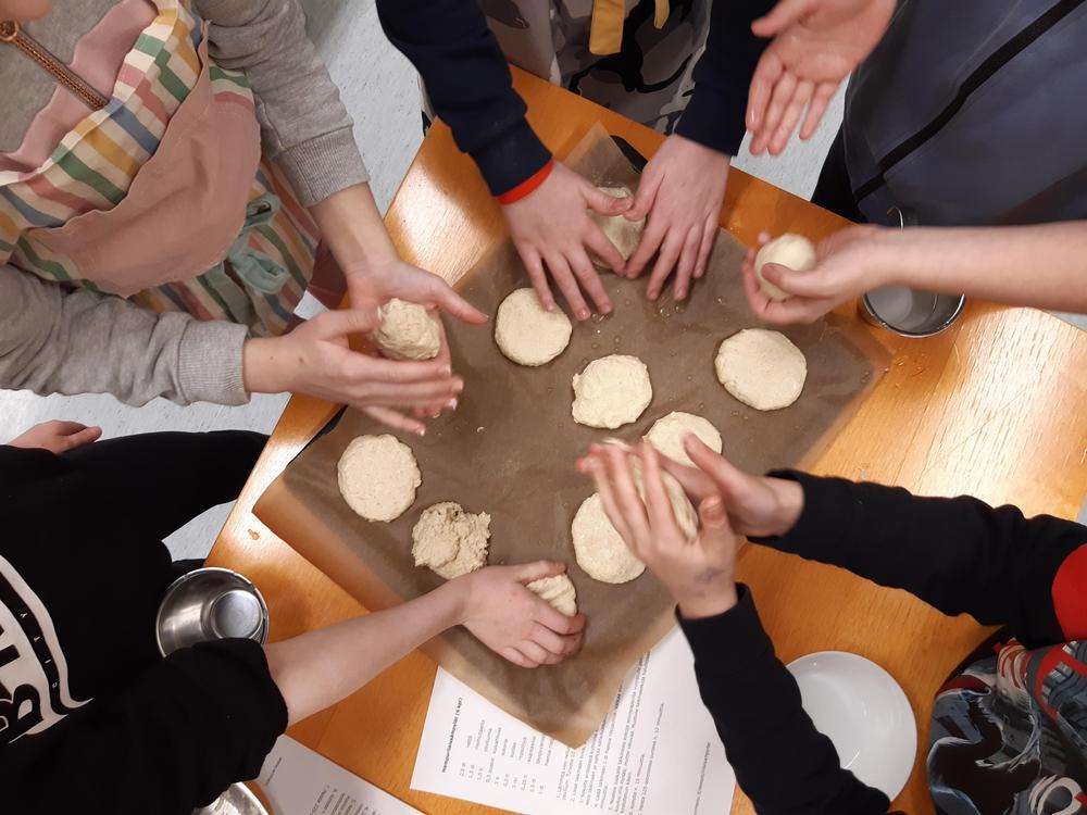 Lasten kädet näkyvät pyörittelevän sämpylätaikinaa leivinpaperin päälle leivontakurssilla.