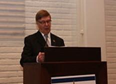 Tummahiuksinen mies juhlavaatteissa puhumassa