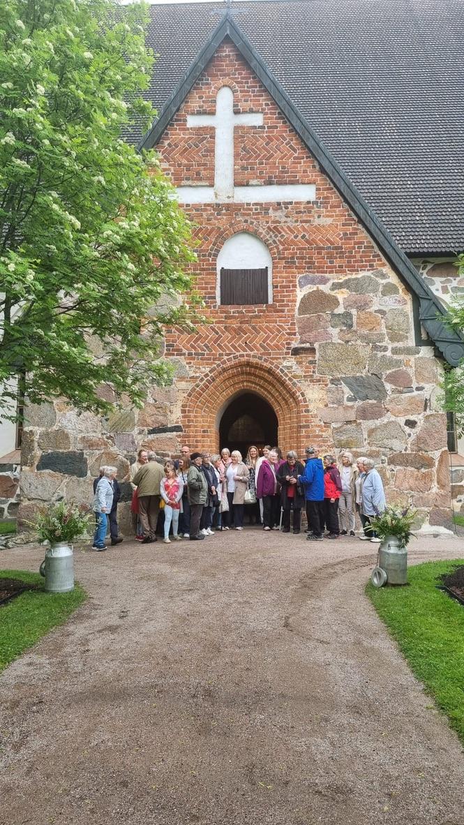 Ryhmä ihmisiä seisomassa ulkona Hollolan keskiaikaisen kivikirkon edessä.