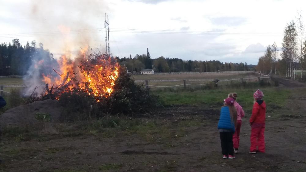 Köyritulet, eli kokko, jota kolme värikkäästi pukeutunutta lasta katsoo pimenevässä syysillassa.