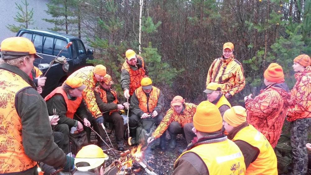 Oranssipukuiset Kinnulan Erämiehet ovat hirvenmetsästyksessä kokoontuneet tauolle paistamaan makkaraa ja syömään eväitä.