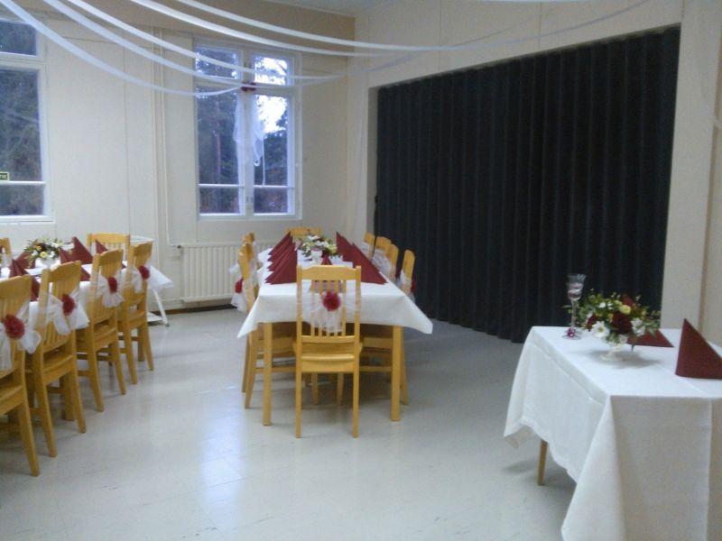 sali, jossa kolme pitkää pöytää, joissa valkoiset pöytäliinat, kattaukset ja tuolit.