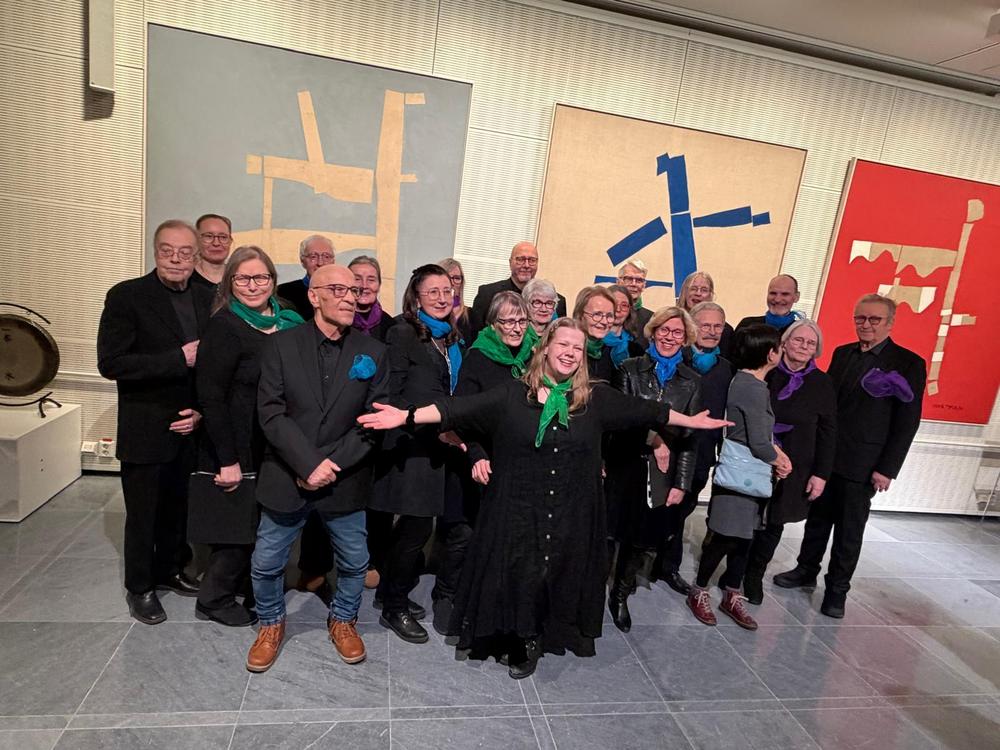 Kuorolaiset mustissa vaatteissa hymyilevät kameralle