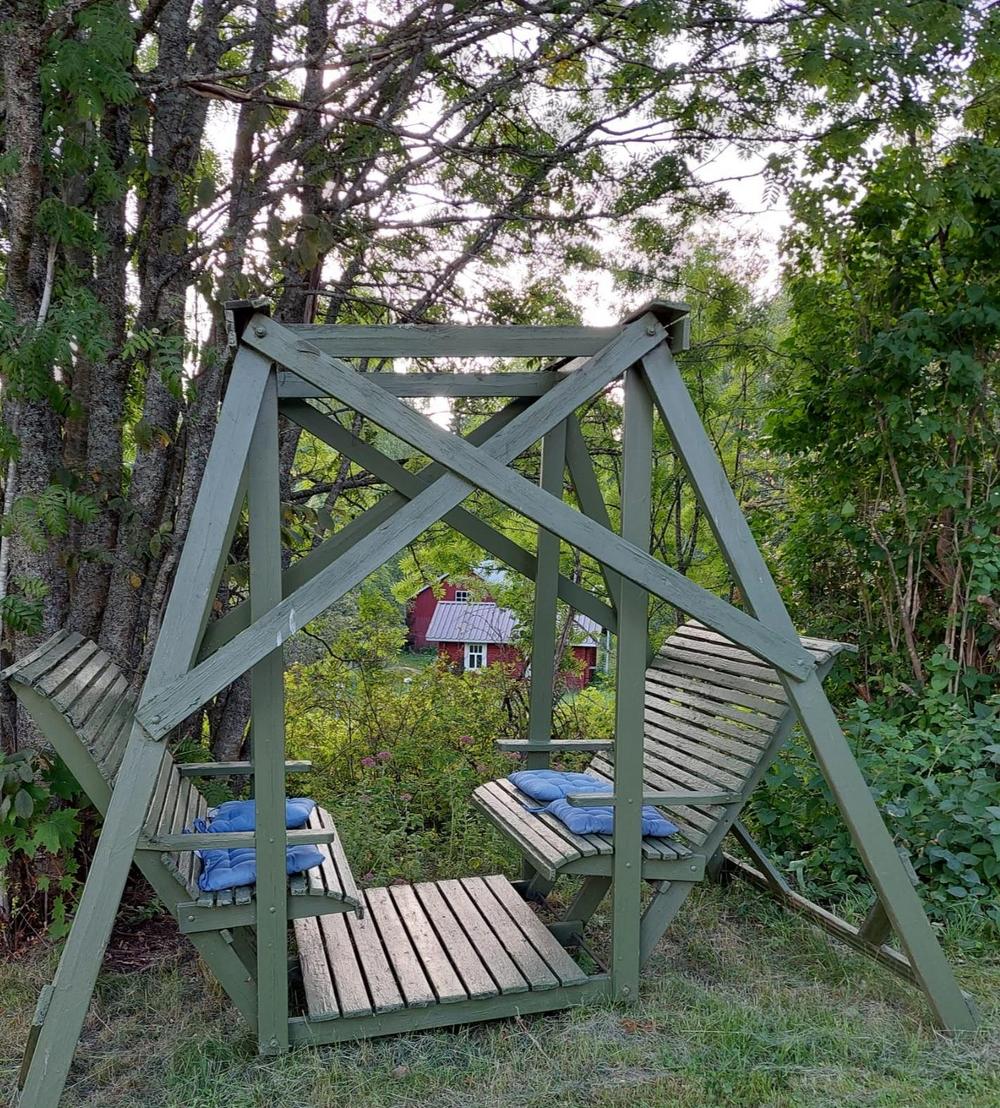 Vihreä kaksipuolinen keinu, takaa näkyy punainen sauna.