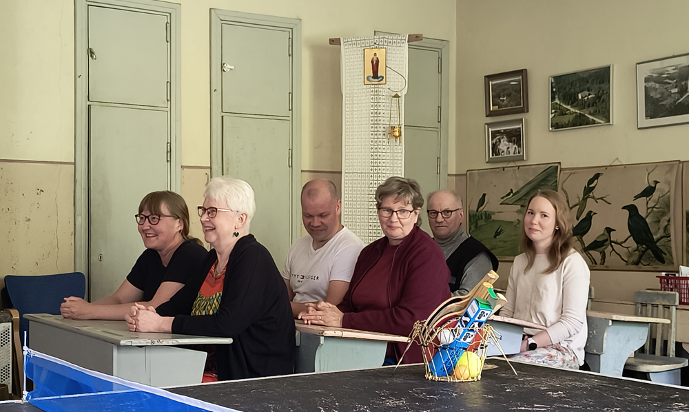 Tuupovaaran kyläyhdistyksen hallituksen jäsenet istuvat pareittain pulpettien takana Ristivaaran vanhalla koululla