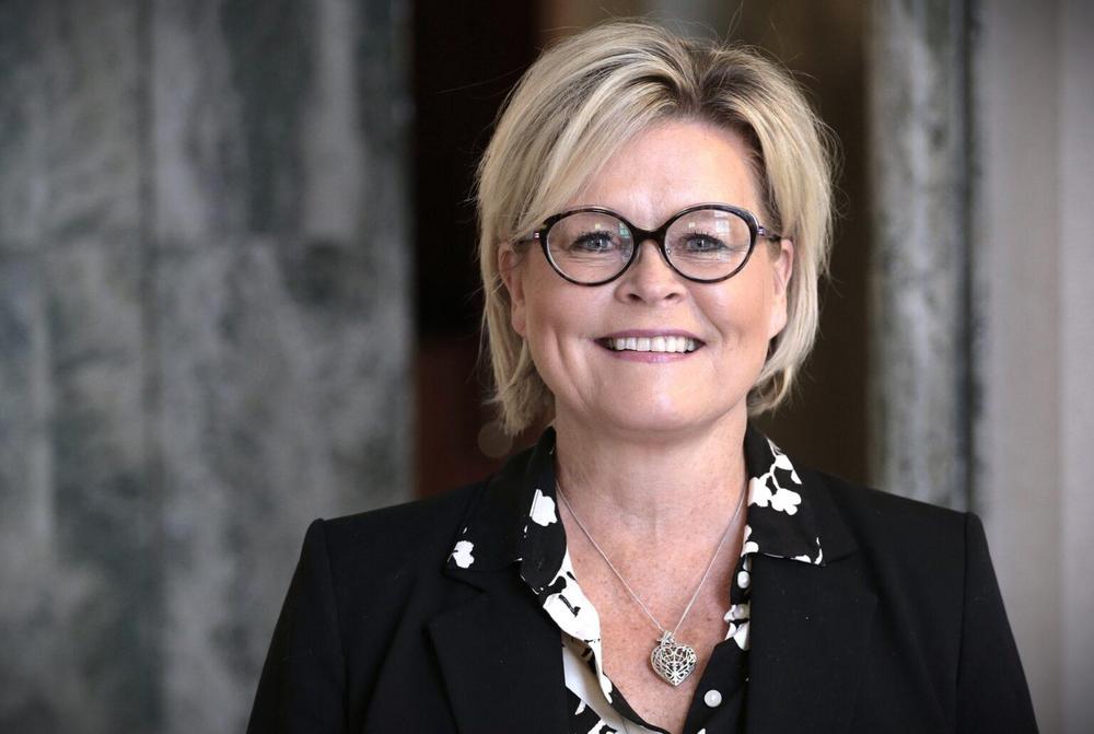 Kansanedustaja Sari Tanus hymyilee kameralle yllään tumma jakku ja sydämenmuotoinen kaulakoru.